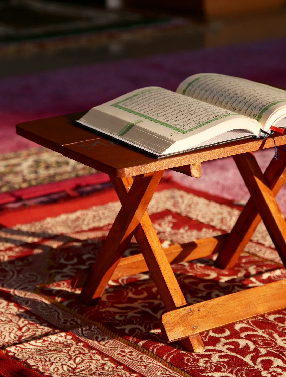 An open Quran resting on a wooden stand in warm sunlight