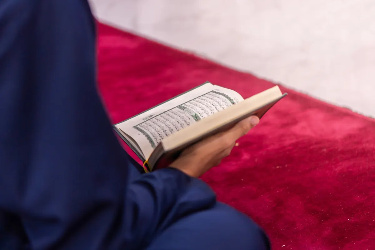 A seated reader holds an open Quran above their lap.