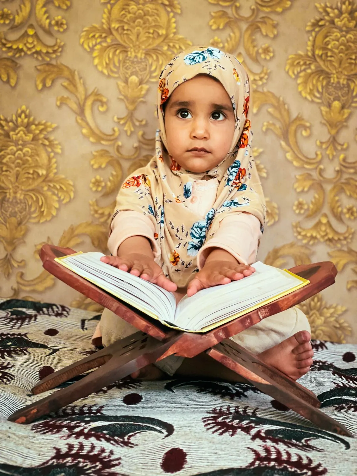A young girl sits behind an open Quran on a wooden stand.
