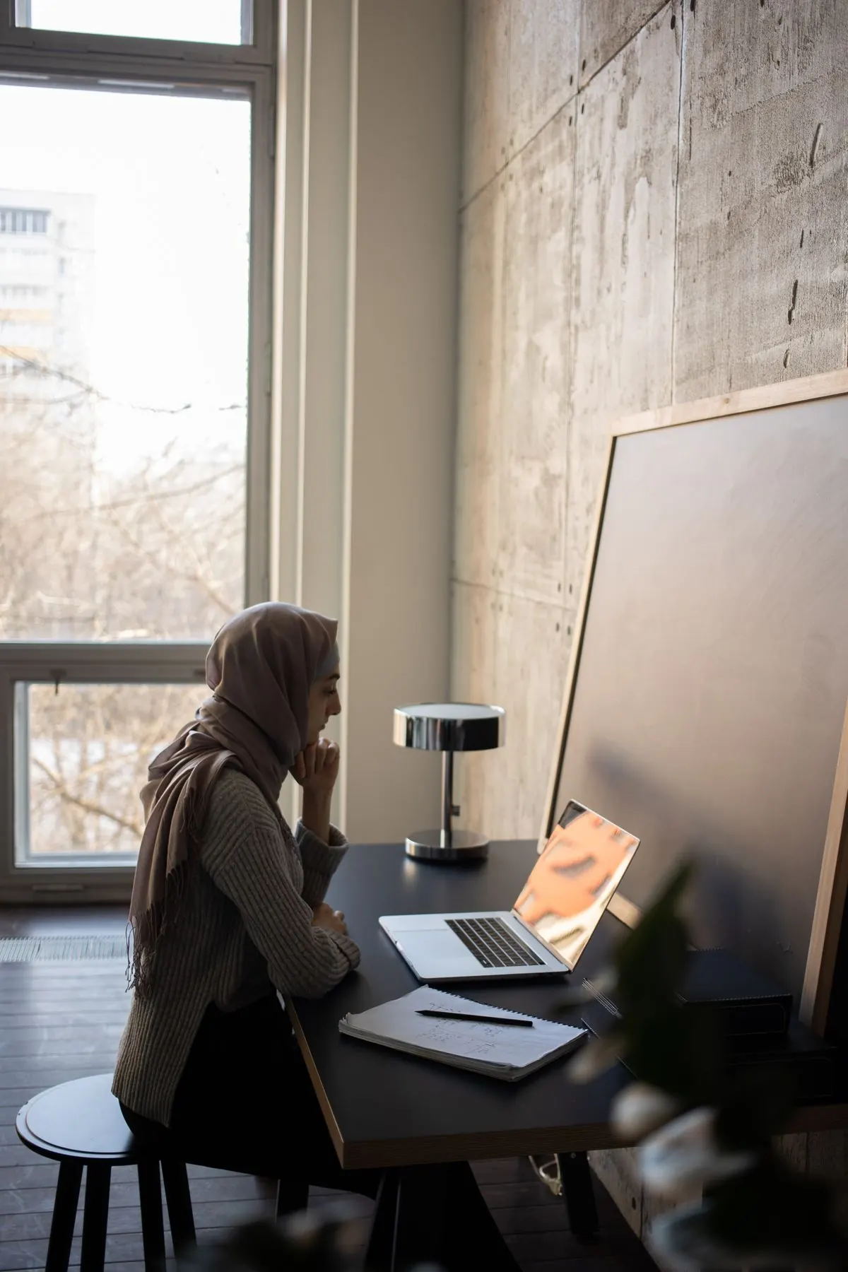 A woman uses a laptop at a desk with a notebook and pen.